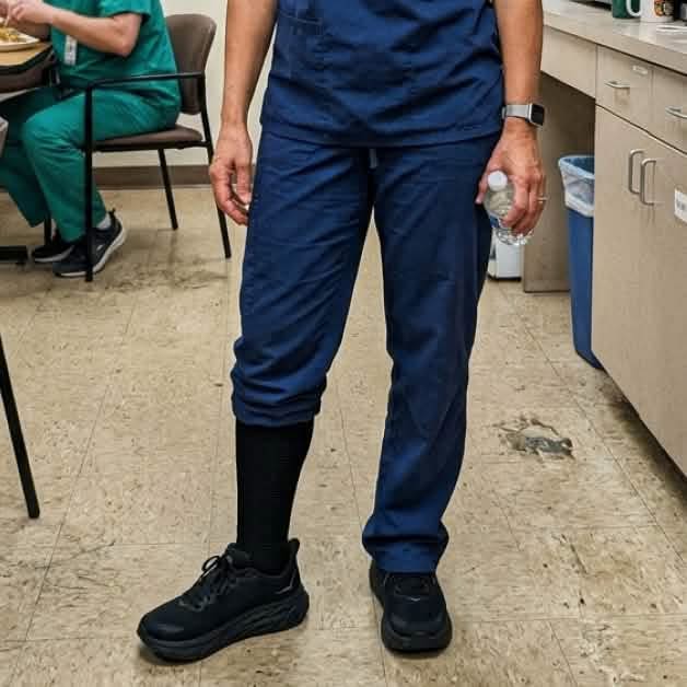 Person in navy scrubs wearing one visible dark compression-style sock.